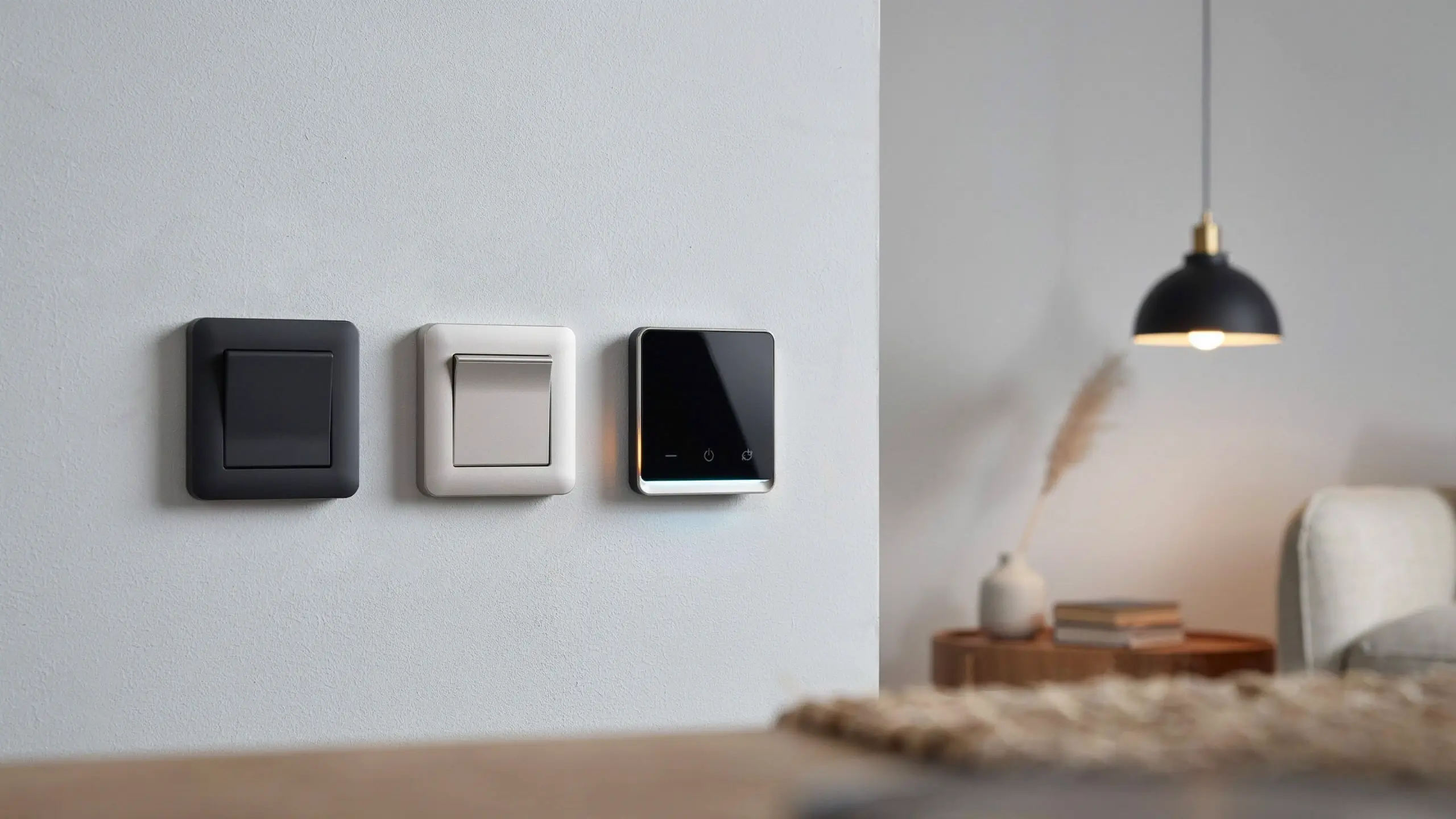Comparison of standard mechanical rocker wall switches in black and white alongside a sleek black glass smart touch panel, illustrating a stylish electrical upgrade for modern living room interiors.