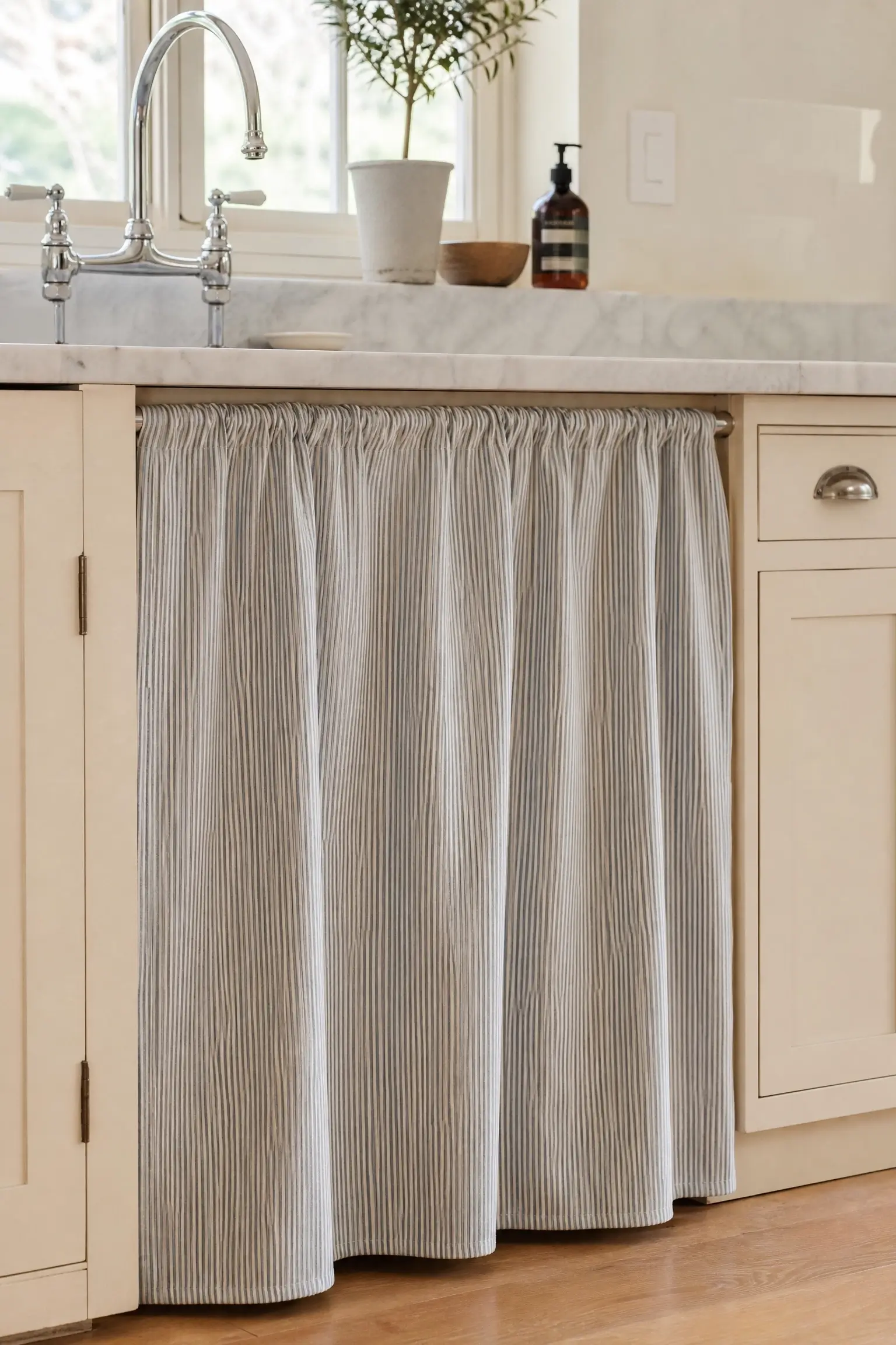 Soft ticking stripe sink cabinet skirt below a marble counter in a cottage kitchen.