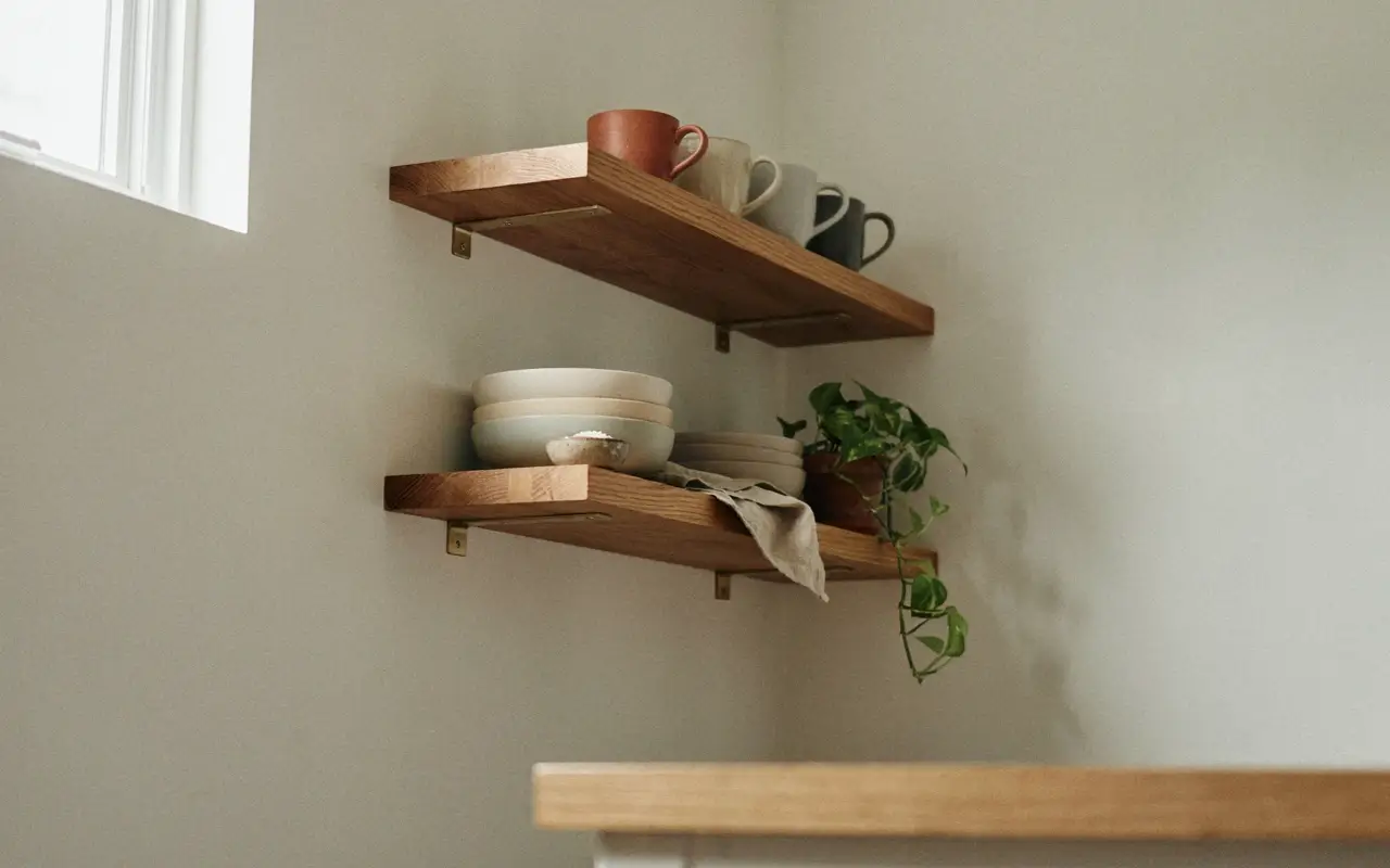 Staggered wood kitchen shelves with mugs, bowls, and a trailing plant in a narrow galley kitchen.