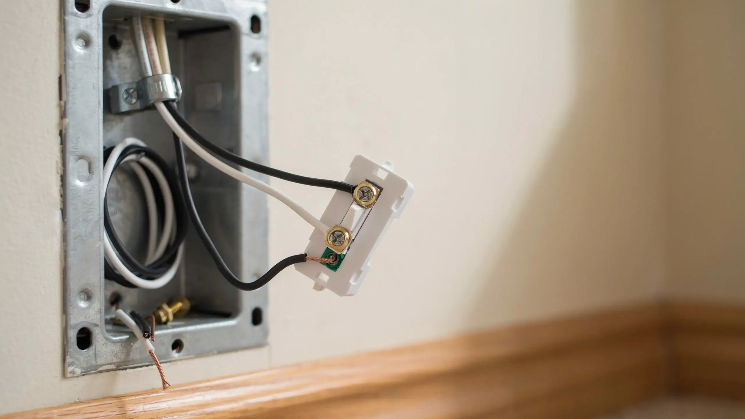White electrical light switch showing a black hot wire and white neutral wire looped around the gold terminal screws, with a copper ground wire hanging loose in a metal junction box during a home DIY installation.
