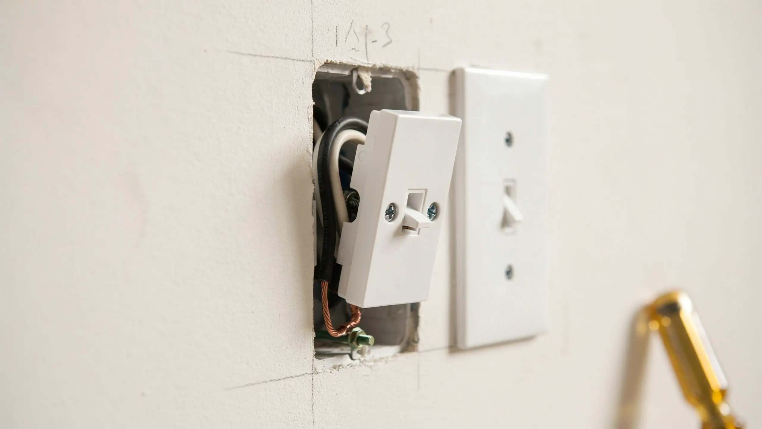 Close-up DIY view of tucking black, white, and copper ground wires into an electrical box while mounting a white toggle switch, using the green grounding screw.