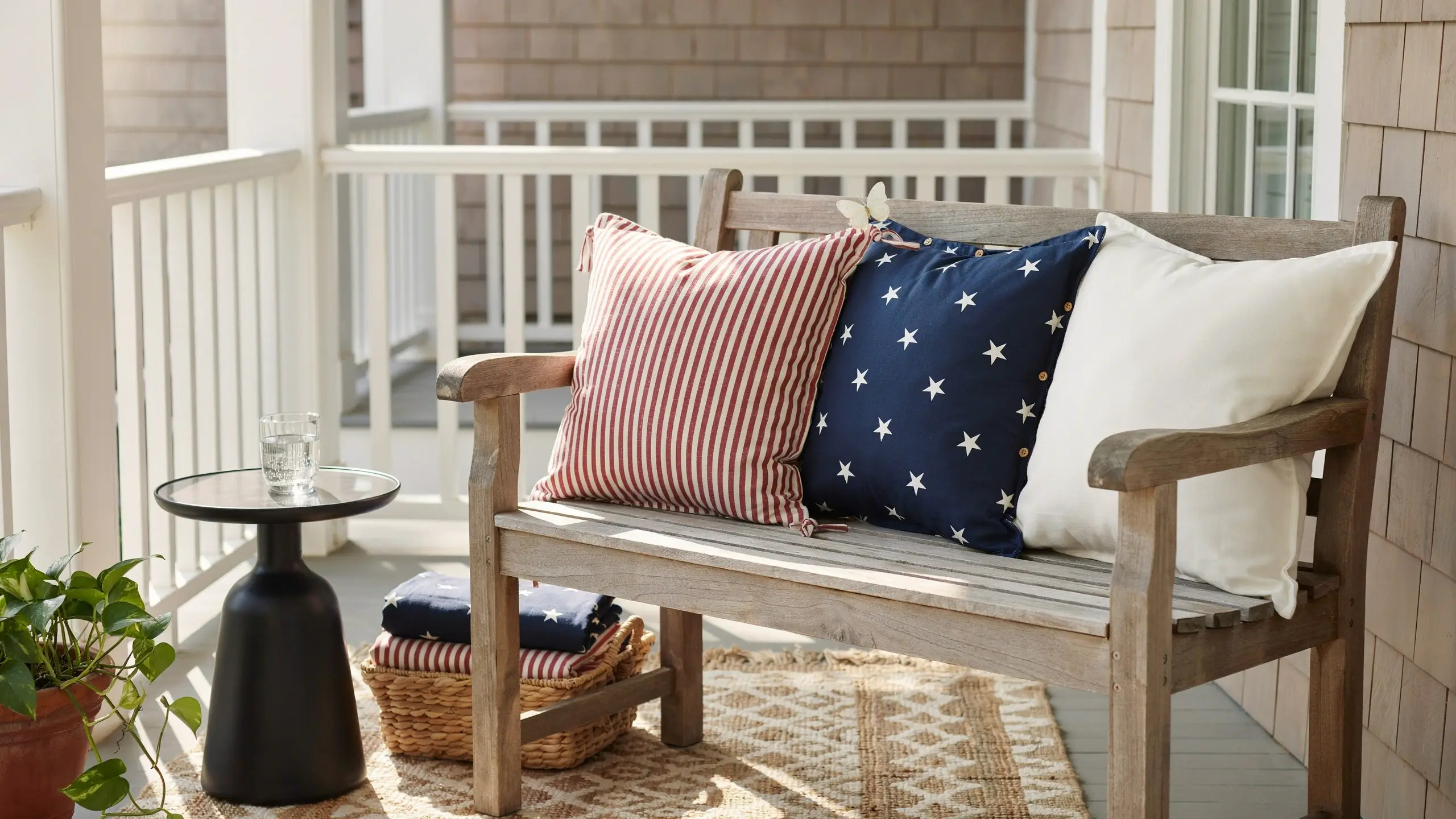 Patriotic striped and star pillow covers styled on a wooden front porch bench.