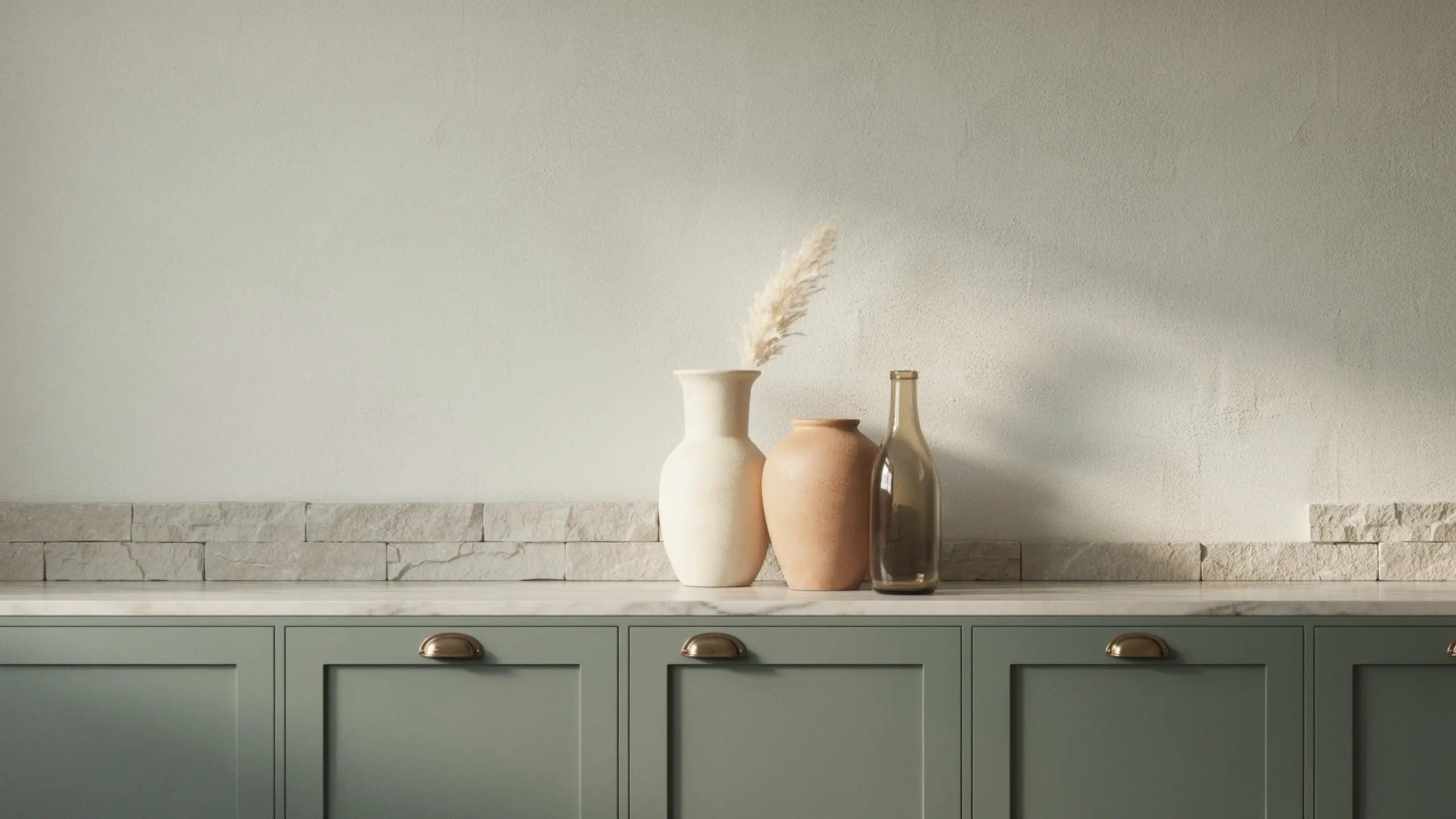 Three oversized neutral vases and urns styled on a countertop above sage green kitchen cabinets.