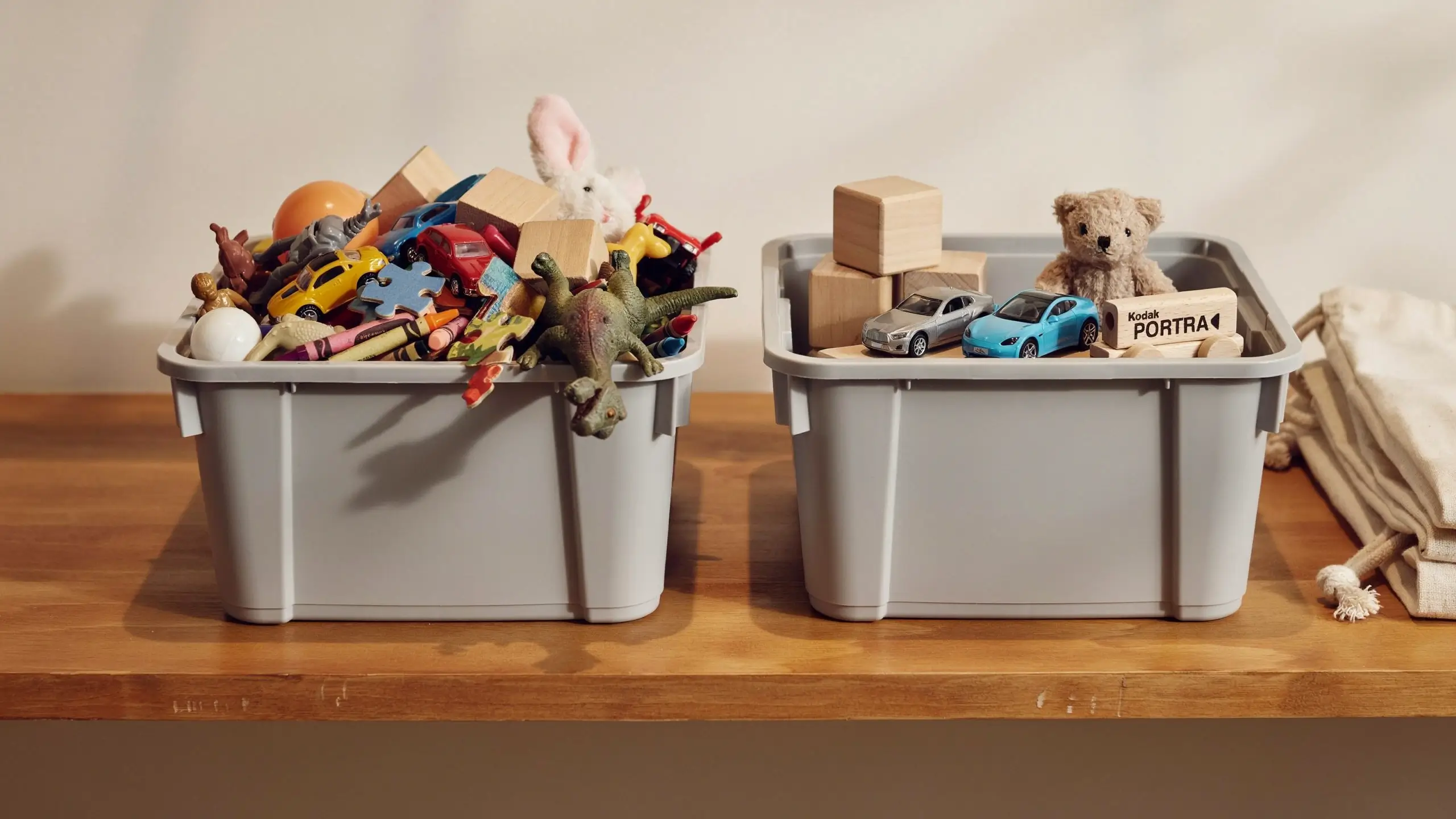 Side-by-side toy organization comparison showing an overflowing messy gray plastic bin next to a neatly organized bin with wooden blocks, silver and blue toy cars, and a teddy bear