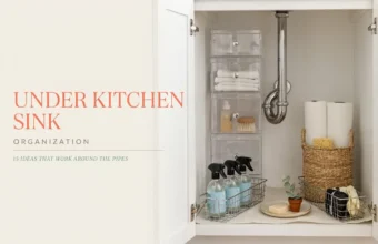 A neatly arranged white cabinet featuring clear acrylic stackable drawers, stainless steel wire baskets holding blue cleaning sprays, and a woven wicker basket for paper towels—all cleverly designed to maximize storage space around the central chrome plumbing pipes.