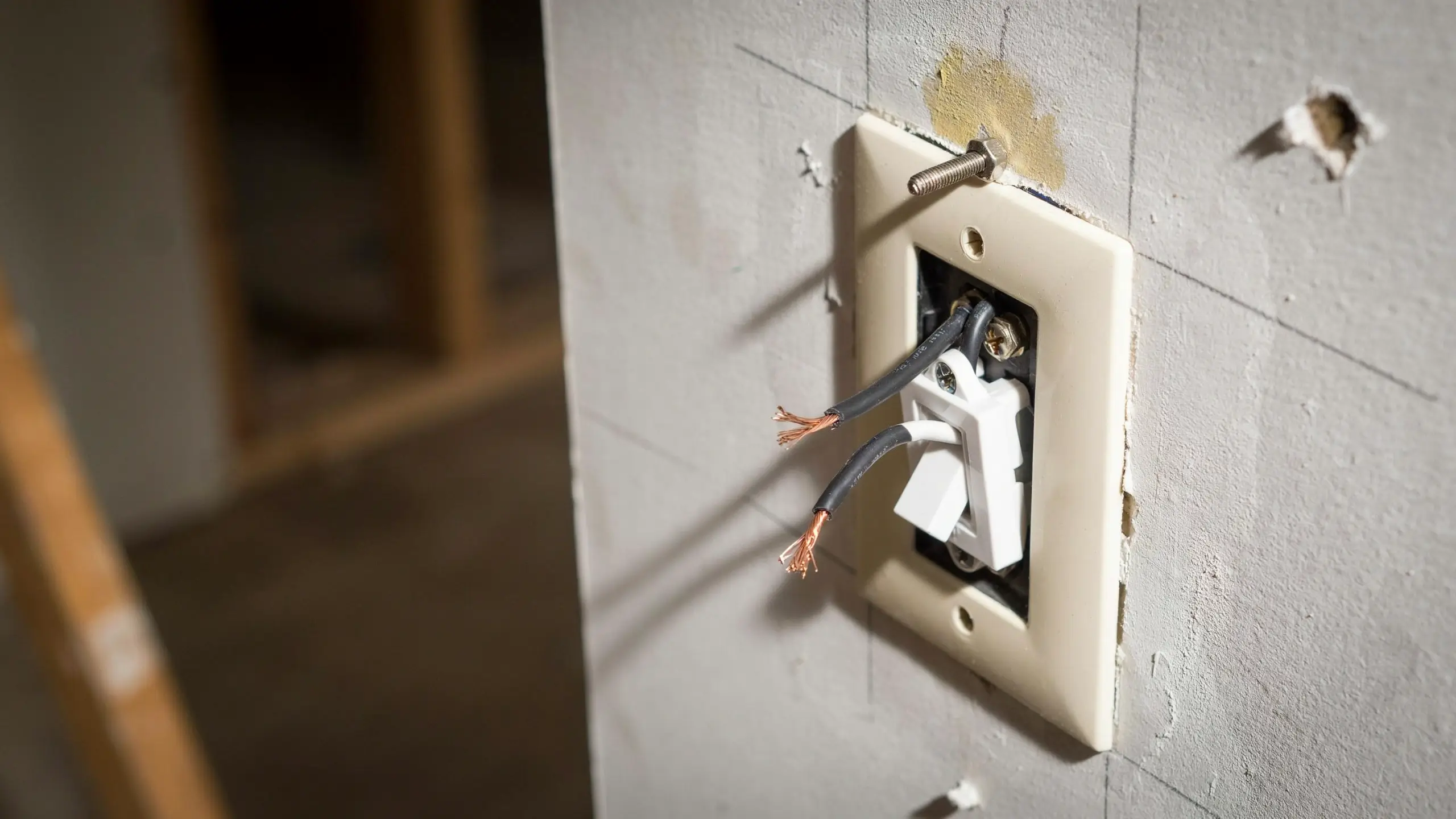 Exposed copper wires and a loose screw on an unfinished DIY wall switch panel, illustrating a common beginner electrical installation error.