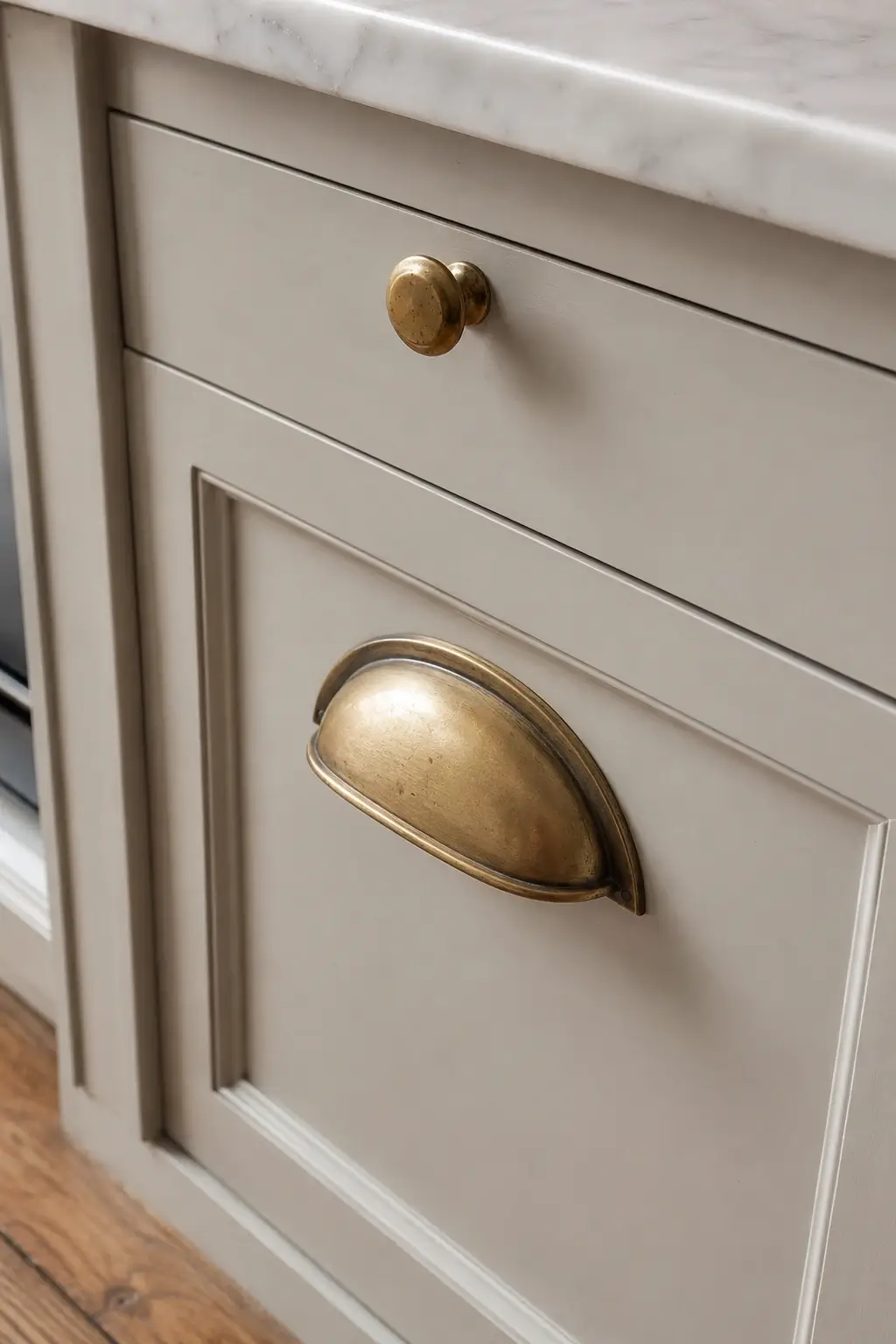 Unlacquered brass knob and bin pull on a warm taupe kitchen cabinet drawer.