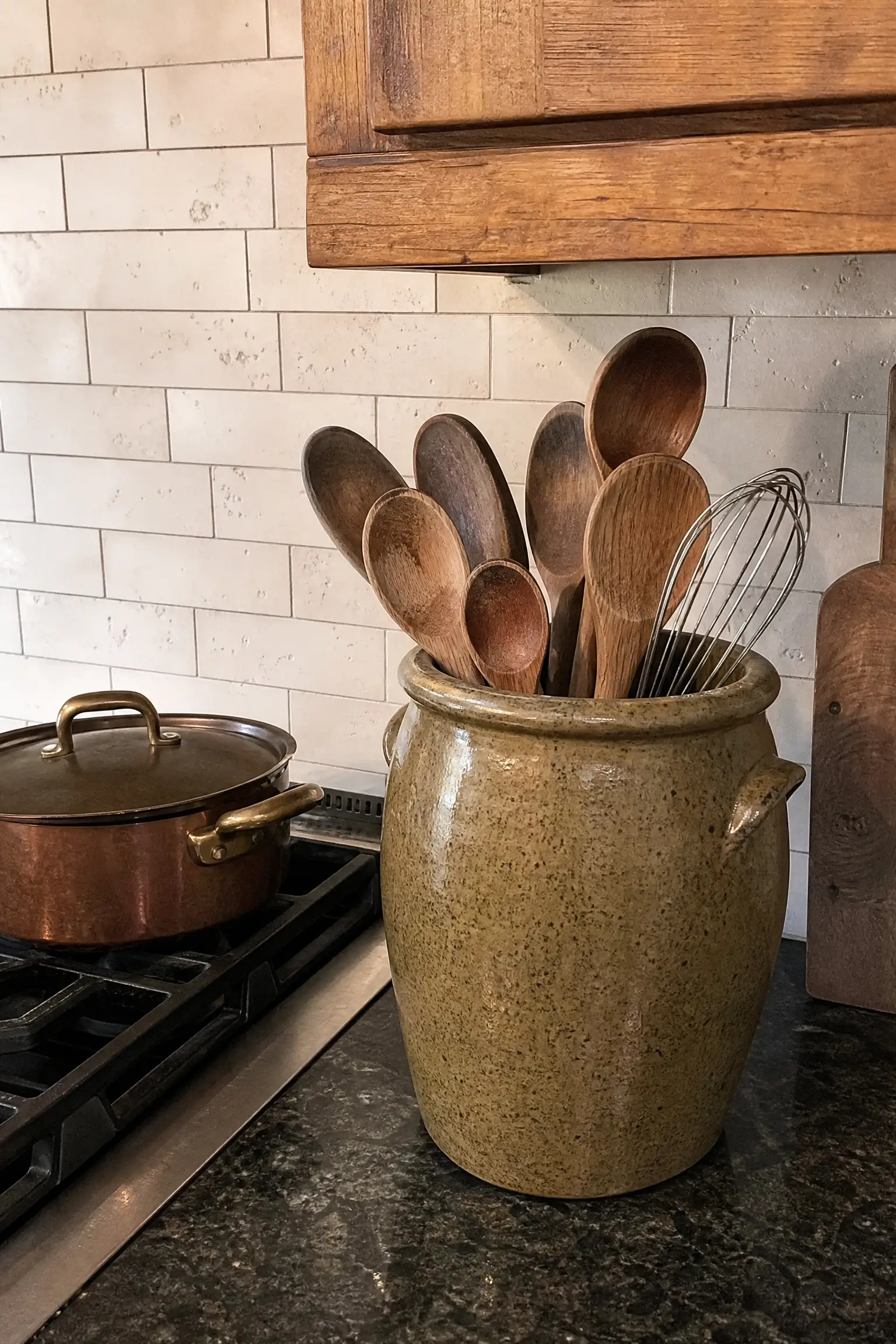 Wooden spoons and a whisk stored in a speckled stoneware crock beside the kitchen stove.