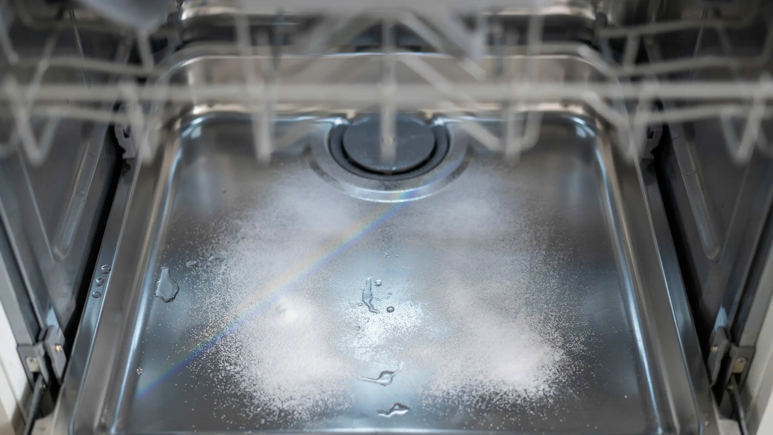 Baking soda powder spread across a stainless steel dishwasher floor to run a short cleaning cycle.