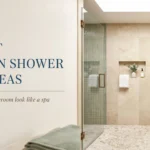 A modern spa bathroom featuring a walk-in shower with beige stone wall tiles, green vertical mosaic accent tiles in a built-in niche, a frameless glass enclosure with brass hardware, and a wooden floating shelf with a trailing green plant.