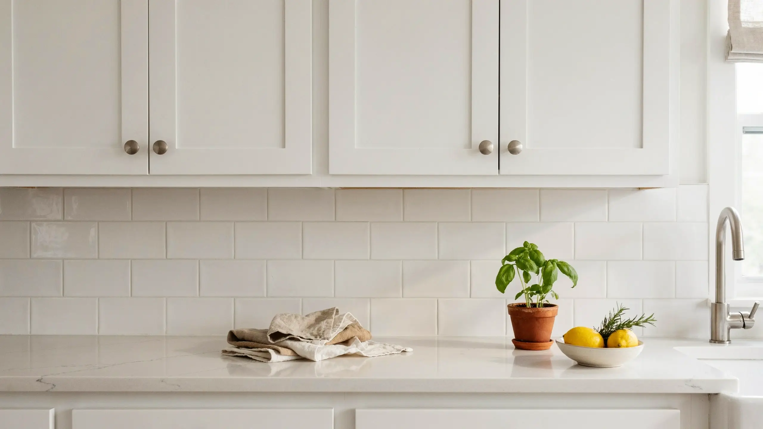 Bright white shaker kitchen with subway tile backsplash, basil plant in terracotta pot, and lemon bowl, contrasting with moody dark kitchen aesthetics.