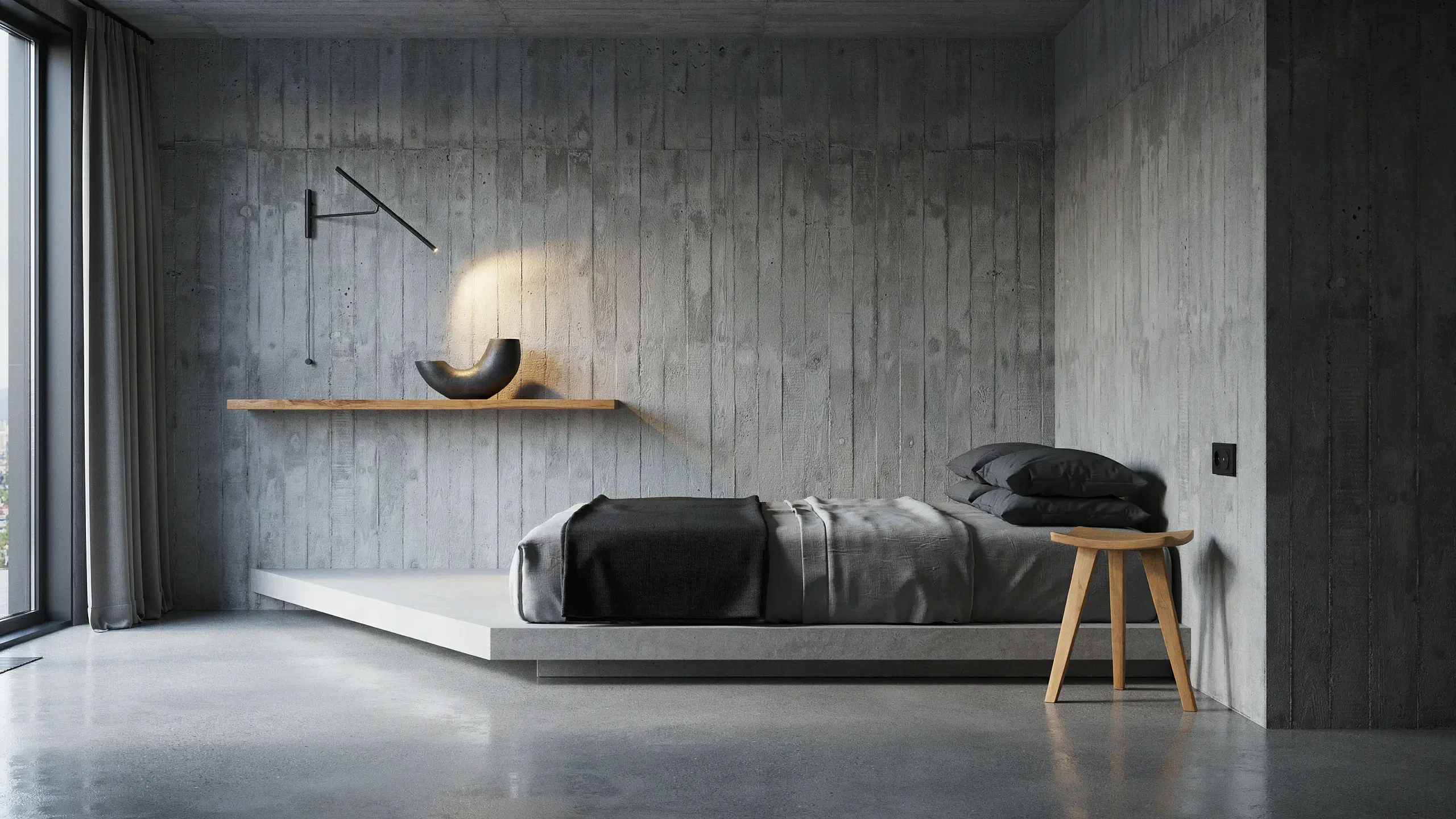Brutalist concrete minimalism bedroom design featuring exposed board-formed concrete walls, a raised concrete platform bed with black duvet and grey sheets, a light wood three-legged stool, and a floating wooden shelf illuminated by a warm spotlight from an angled black wall sconce.