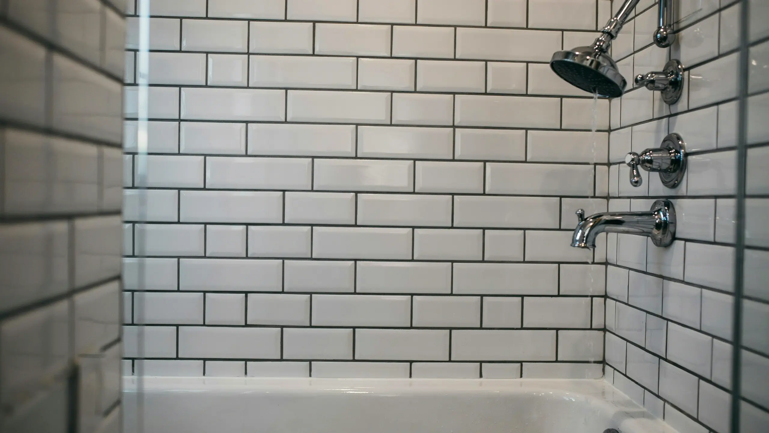 Classic white subway tile shower wall with contrasting black grout, paired with polished chrome showerhead and bathtub spout.