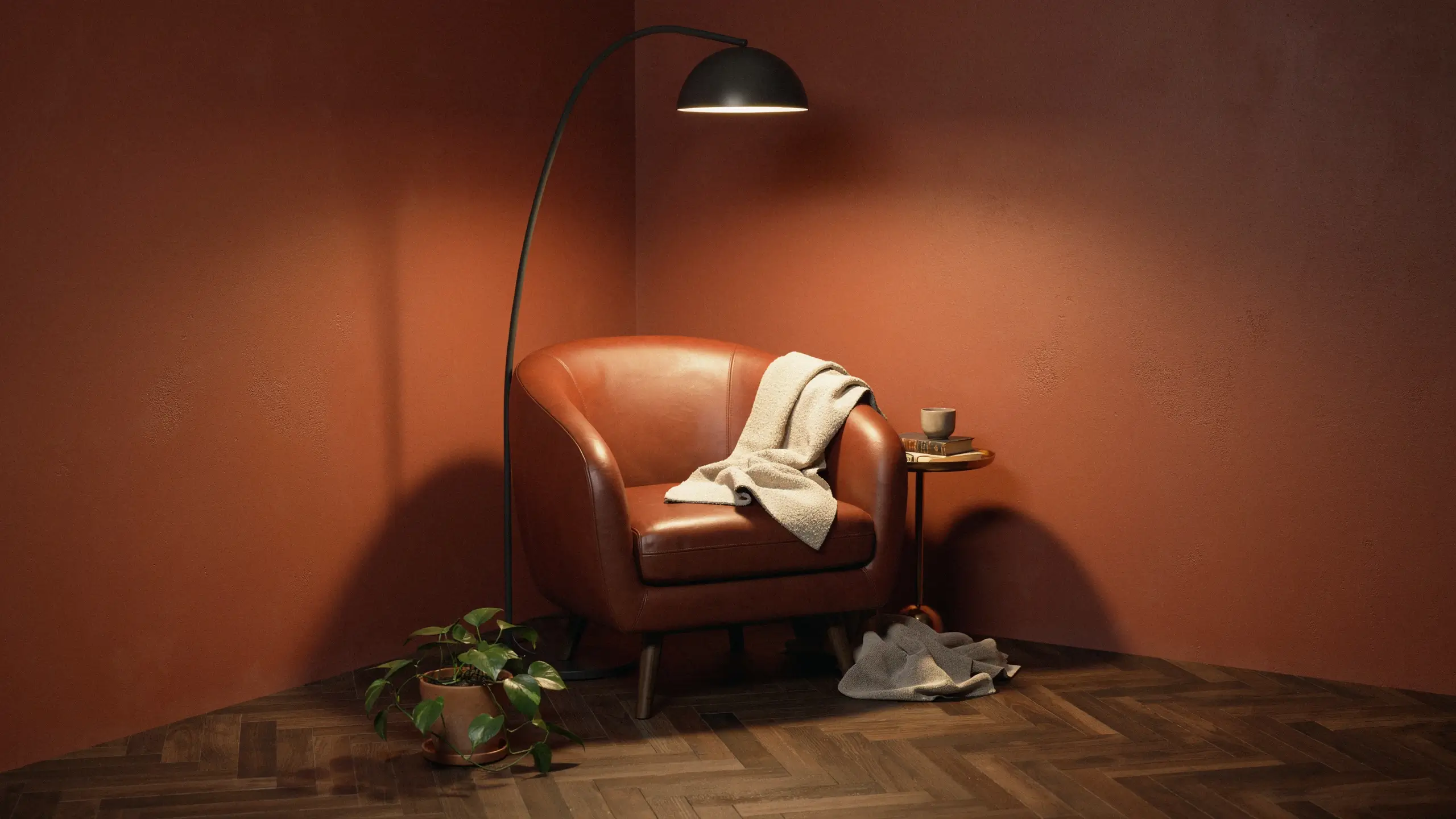 Cozy terracotta reading corner with a brown leather accent chair, draped throw blanket, black arc floor lamp, and potted plant on herringbone wood.