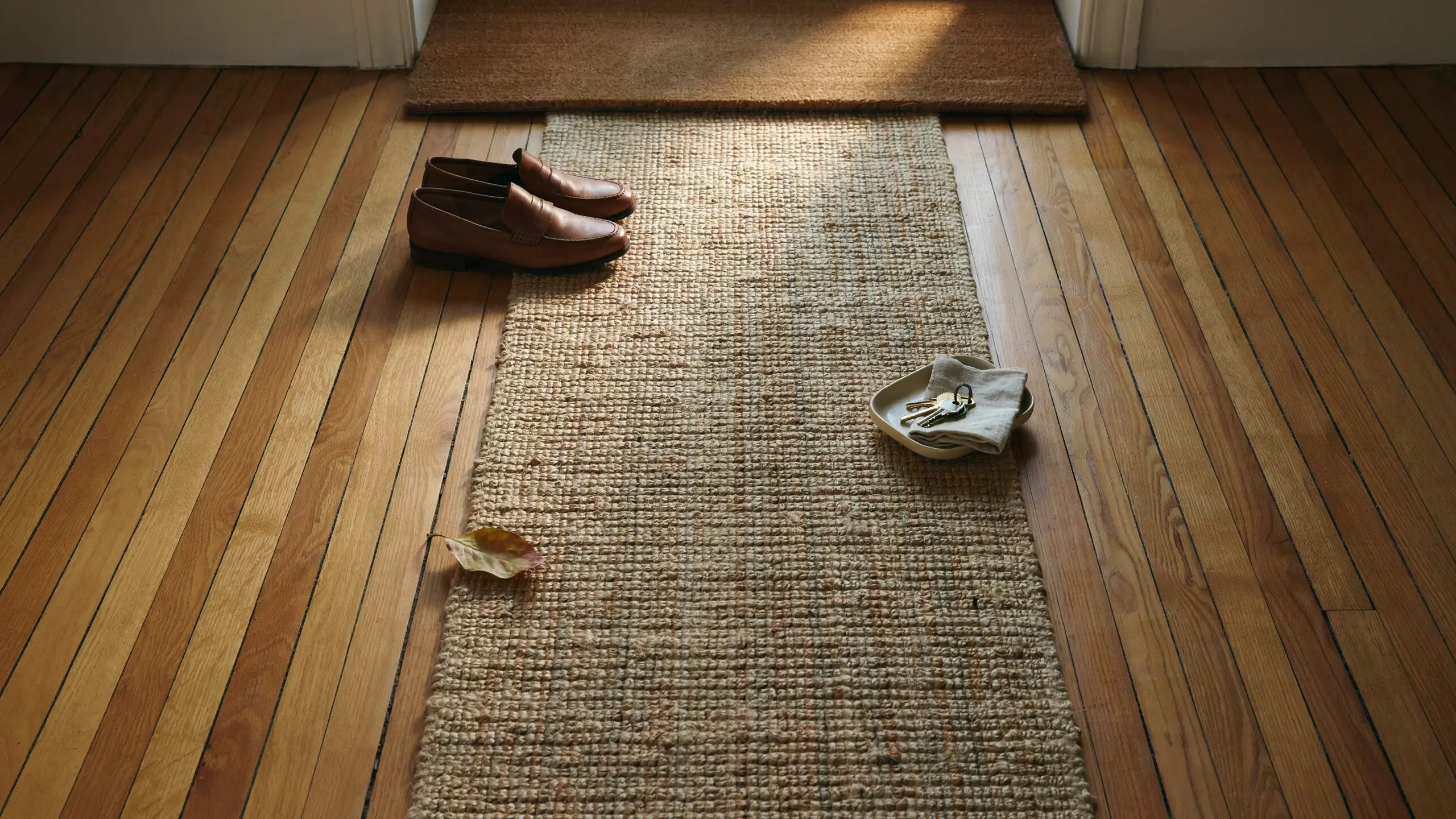 Durable woven jute runner rug protecting a hardwood entryway floor, styled with brown leather loafers and an everyday keys drop zone.