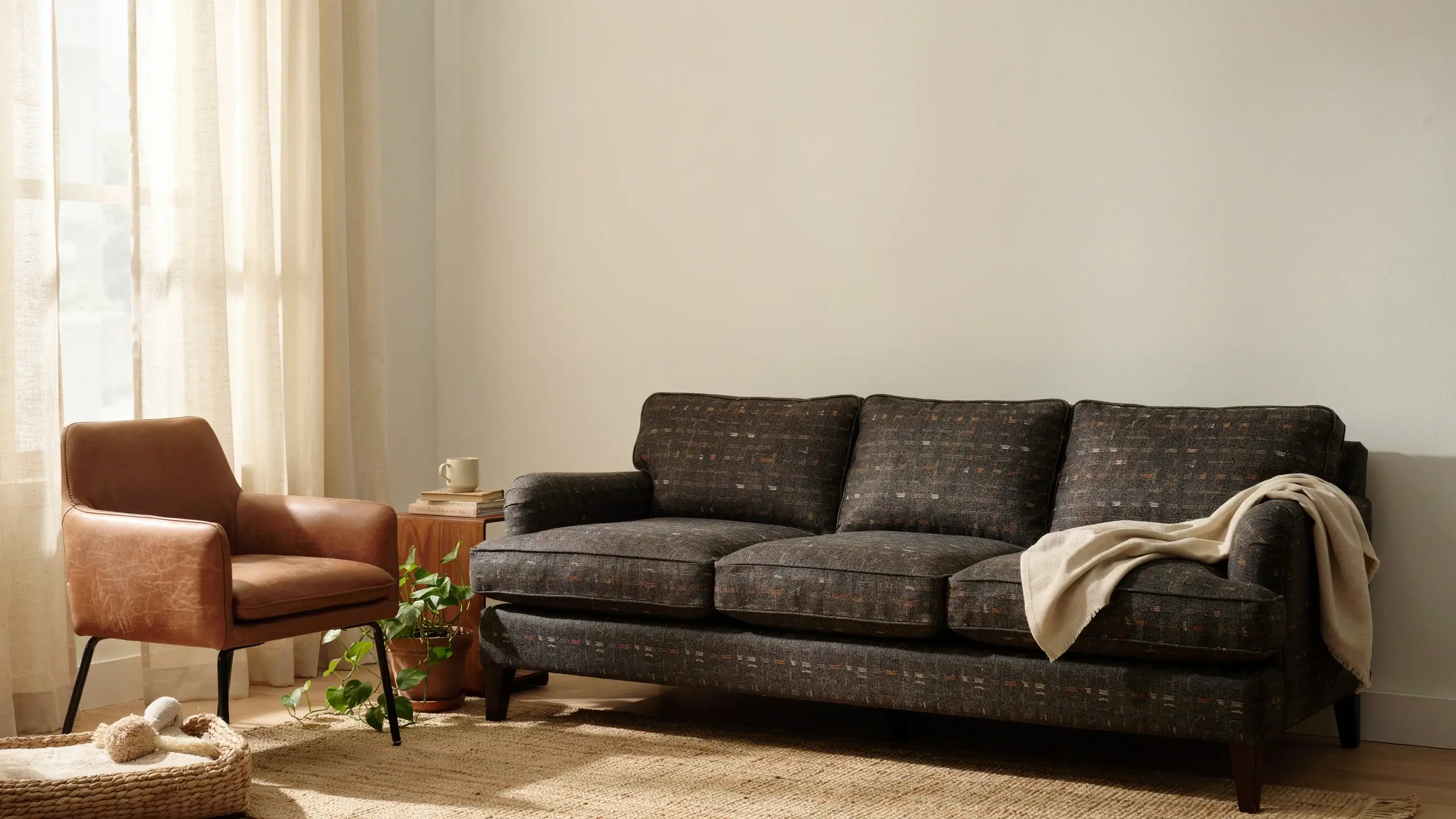 A durable dark patterned sofa and brown leather armchair in a sunlit living room, featuring mess-resistant upholstery and a jute rug ideal for hiding daily stains.