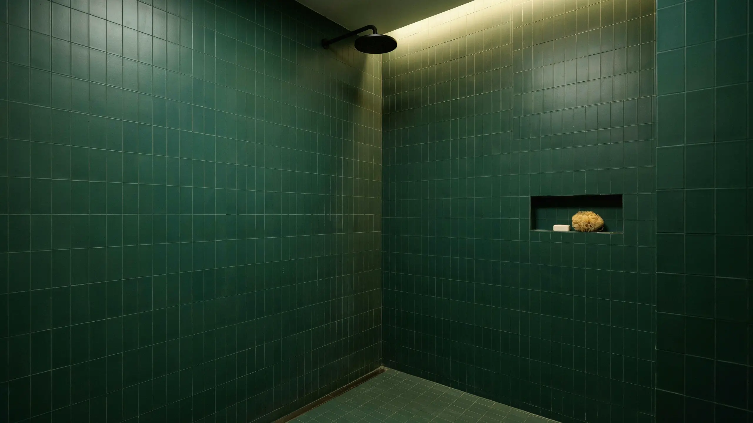 Modern walk-in shower with dark forest green square tiles, a matte black rain showerhead, and a recessed built-in niche displaying a natural sea sponge and bar of white soap.