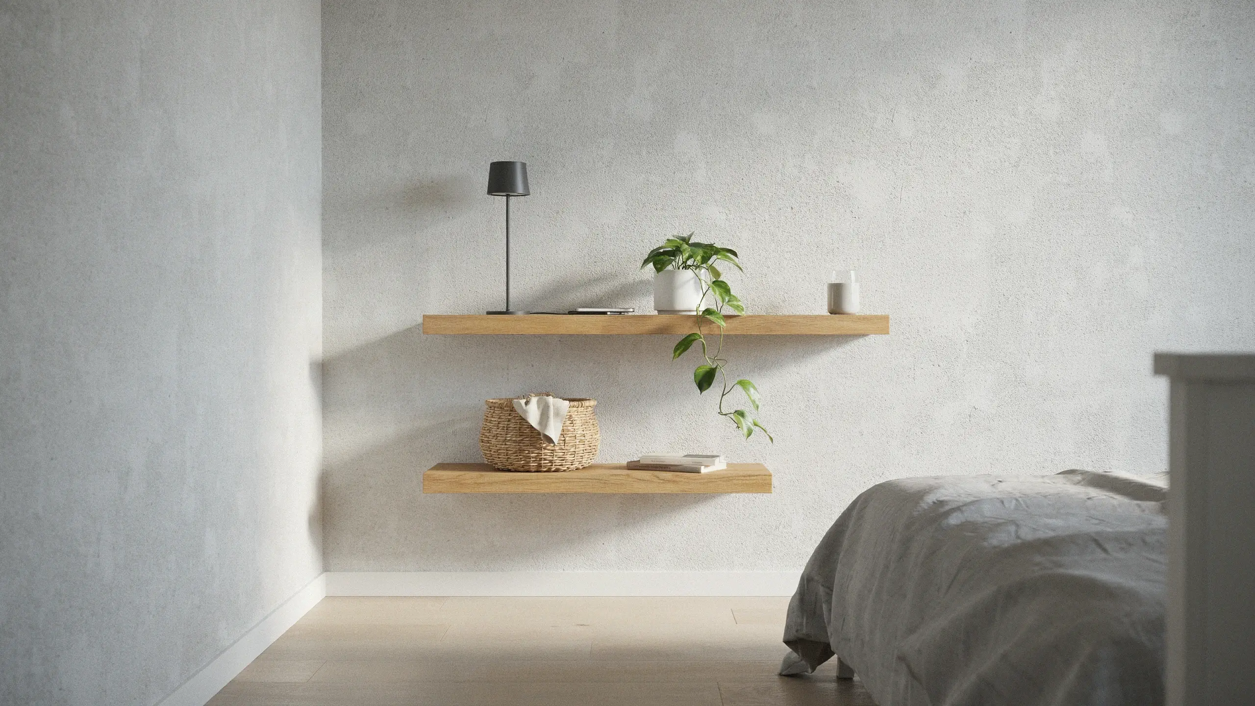 Two floating wooden wall shelves on a light gray textured wall holding a black lamp, potted vine plant, woven basket, and books beside a bed.