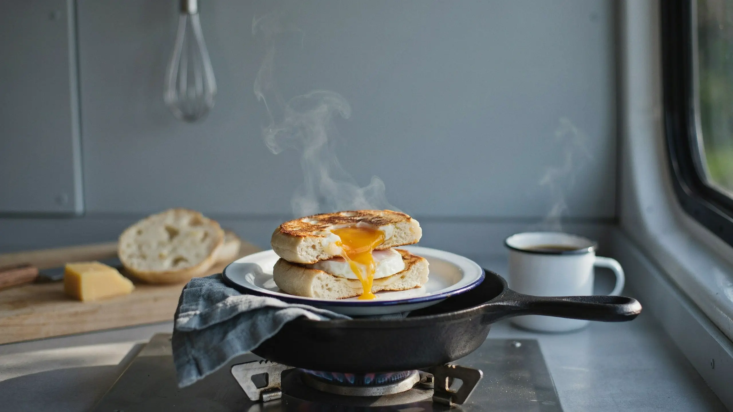 Hot English muffin breakfast sandwich with melted cheese and a runny egg yolk resting on a cast iron skillet.