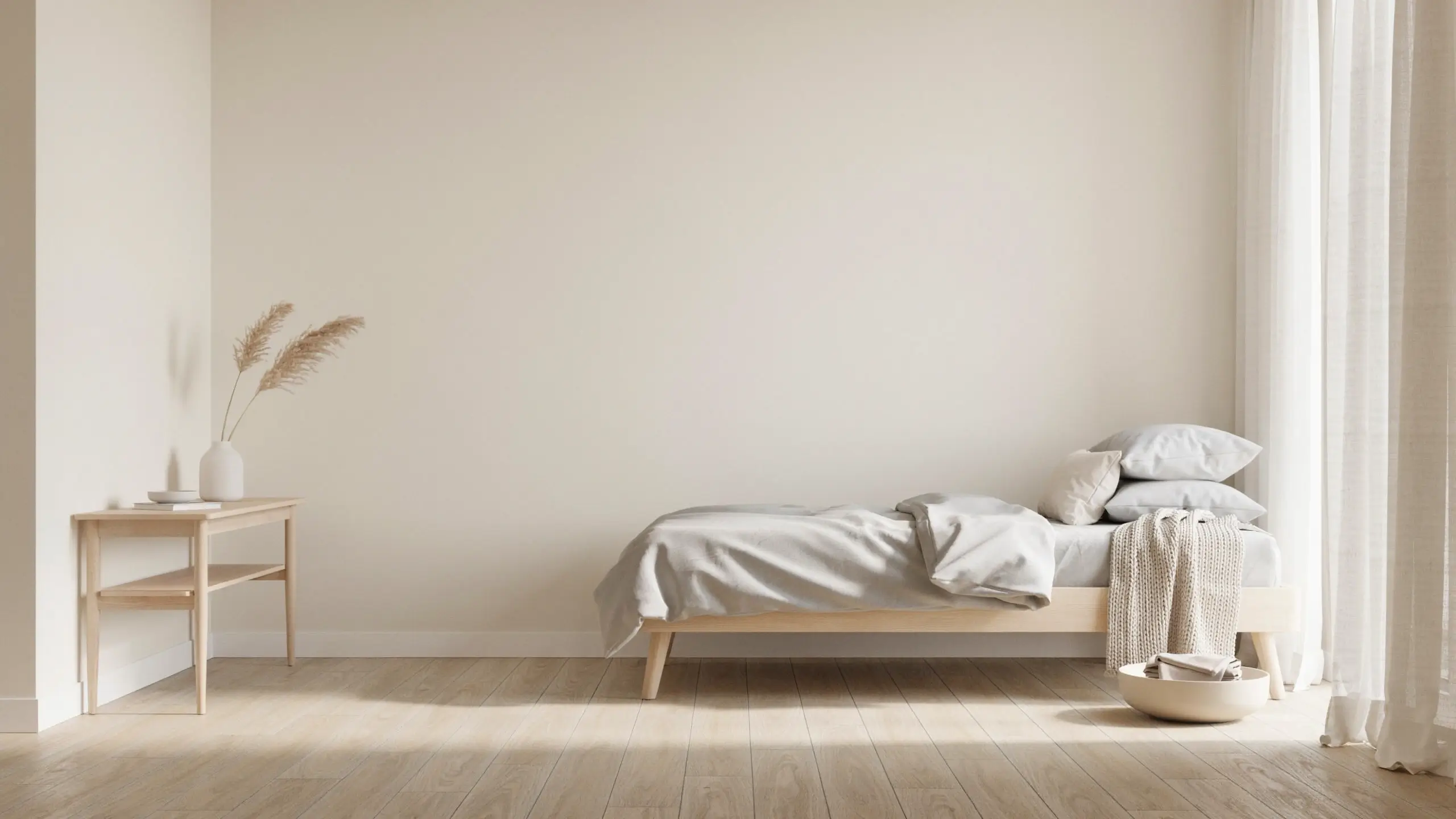 Light minimalist bedroom with low wooden bed frame and simple side table holding pampas grass.