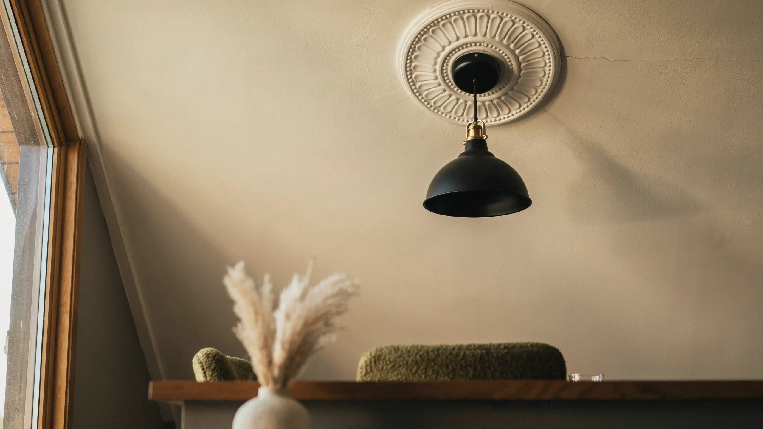 Matte black dome pendant light with brass fixture hanging from a white ornate ceiling rose on a sloped attic wall.