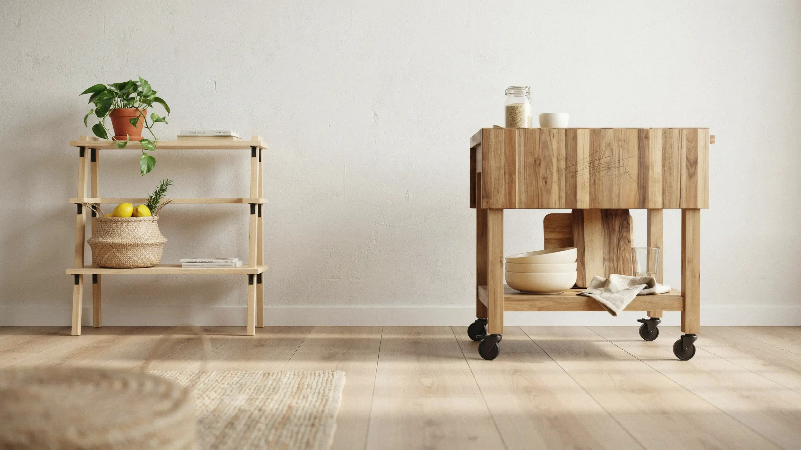 Renter-friendly freestanding wooden open shelf unit with a potted plant, books, and a lemon basket, next to a rolling kitchen cart with white bowls on black caster wheels in a bright, neutral room.