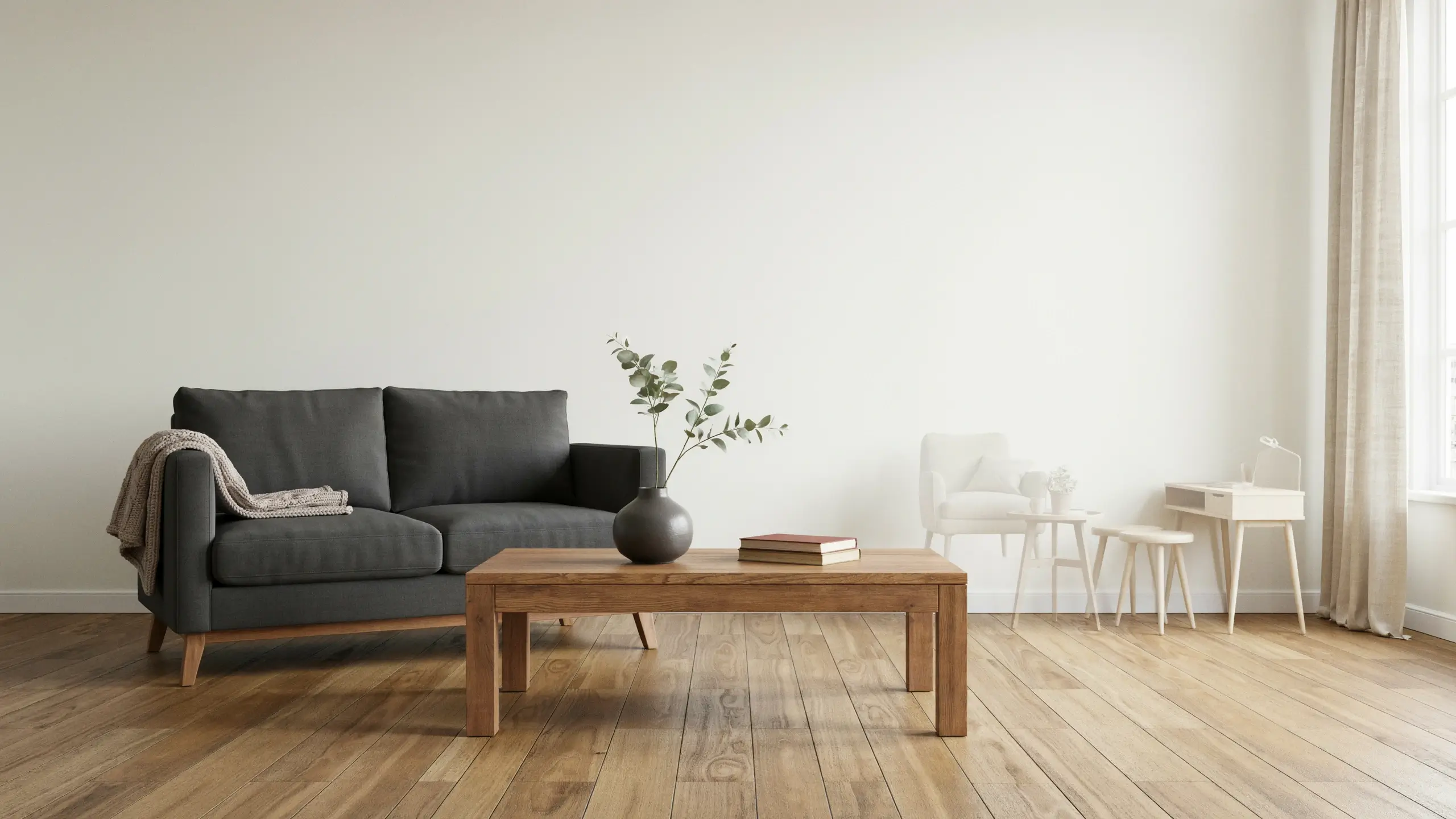 A minimalist Scandinavian living room anchored by a large dark grey sofa and a substantial wooden coffee table, demonstrating the interior design principle of choosing fewer, bigger furniture pieces over a bunch of small ones to reduce visual clutter and create an airy, open atmosphere.