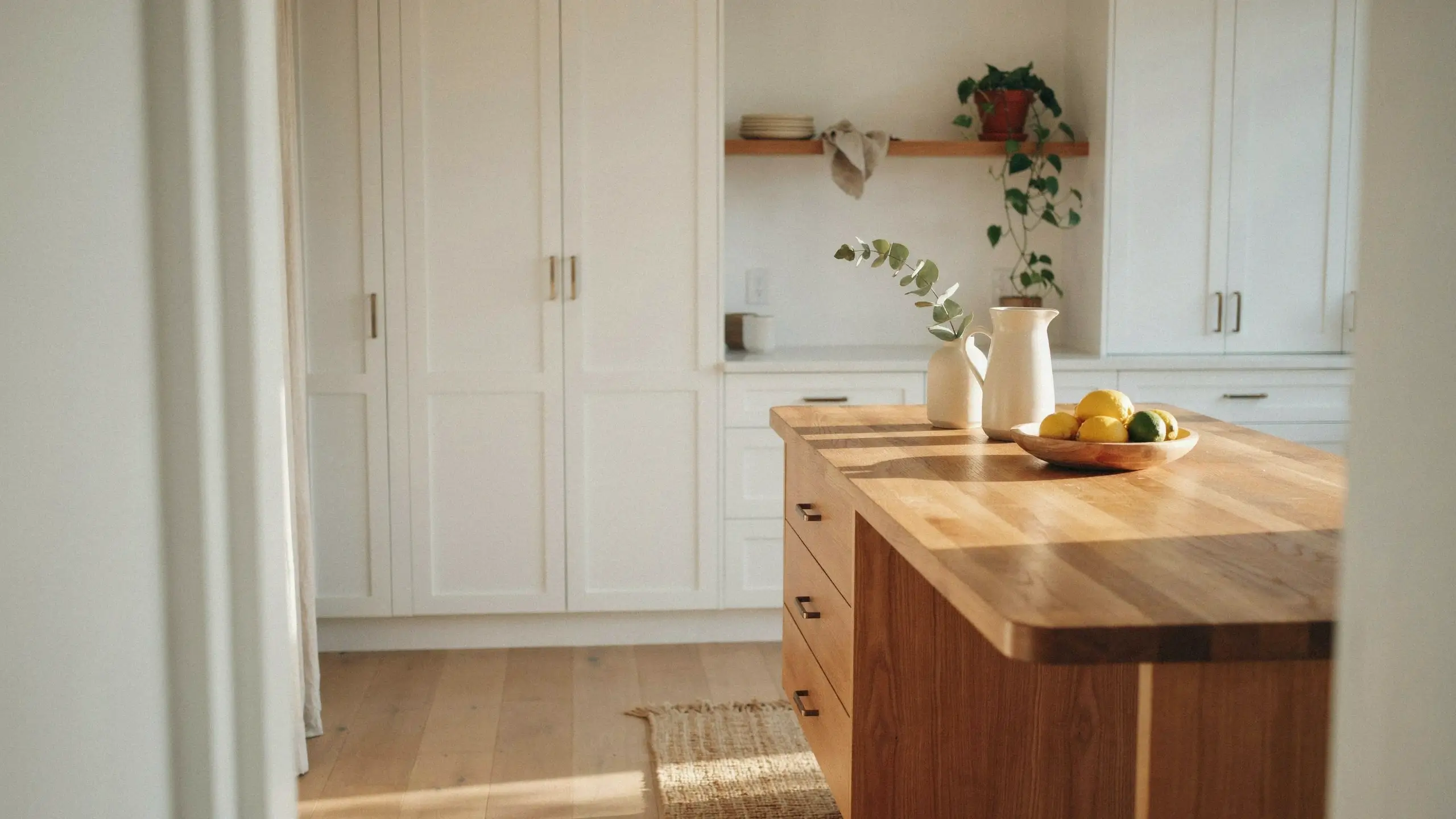 Sunlit white kitchen interior mixing a warm wood island with painted shaker cabinets, styled with fresh lemons and eucalyptus.