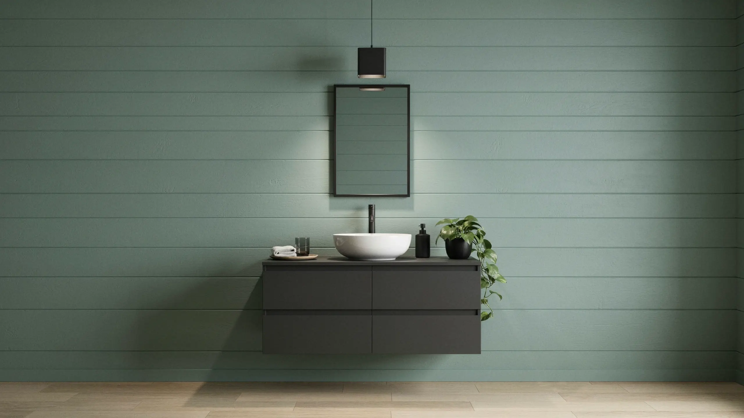 Modern bathroom vanity featuring a matte black floating cabinet with two large drawers, a white round vessel sink, and a matte black wall-mounted faucet. The minimalist setup is styled with a black rectangular mirror, a matching black pendant light, and a trailing green potted plant against a horizontally paneled sage green wall and light wood flooring.