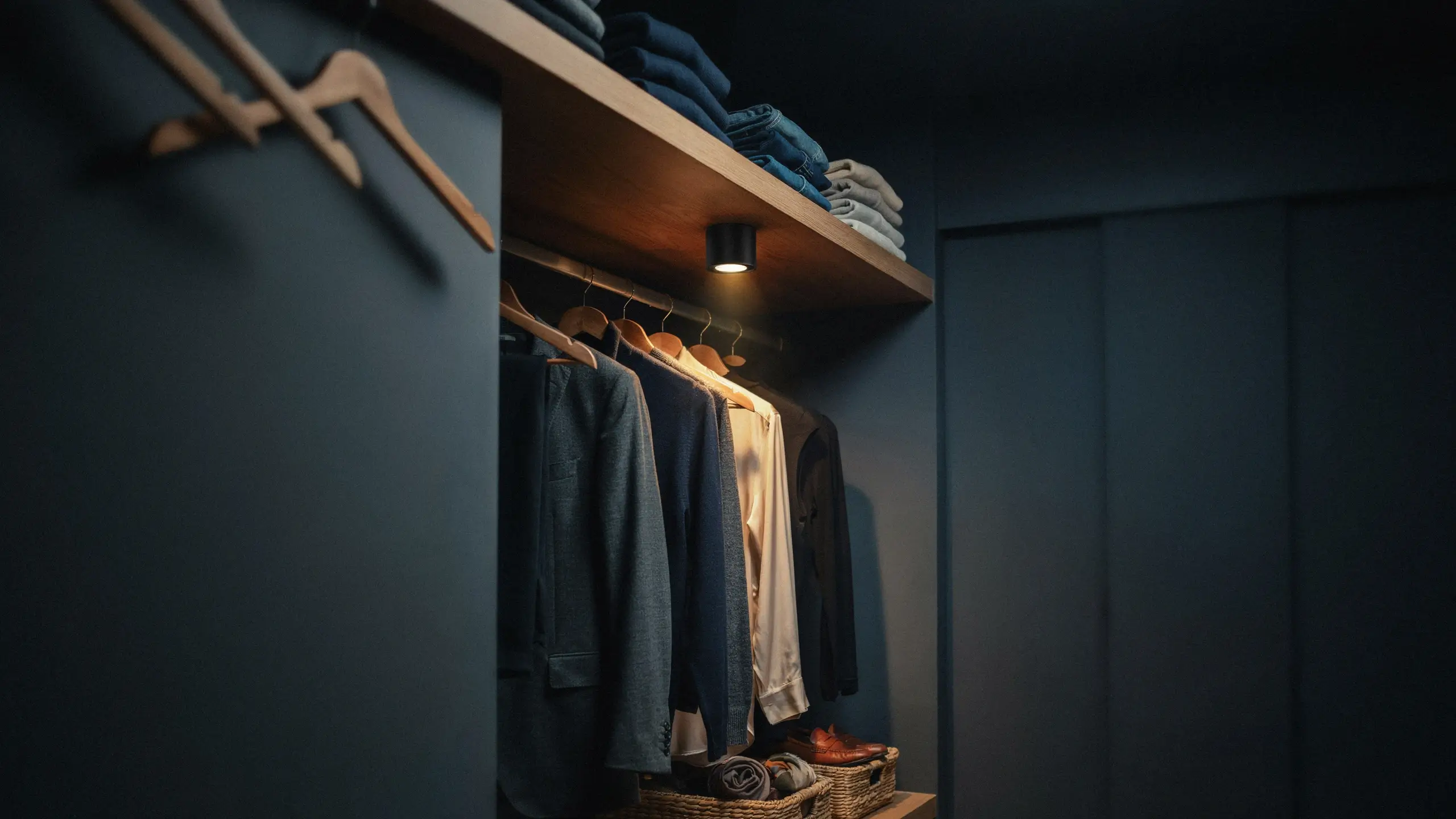 Modern dark blue walk-in closet with a focused spotlight illuminating hanging suits and a white shirt on wooden hangers.