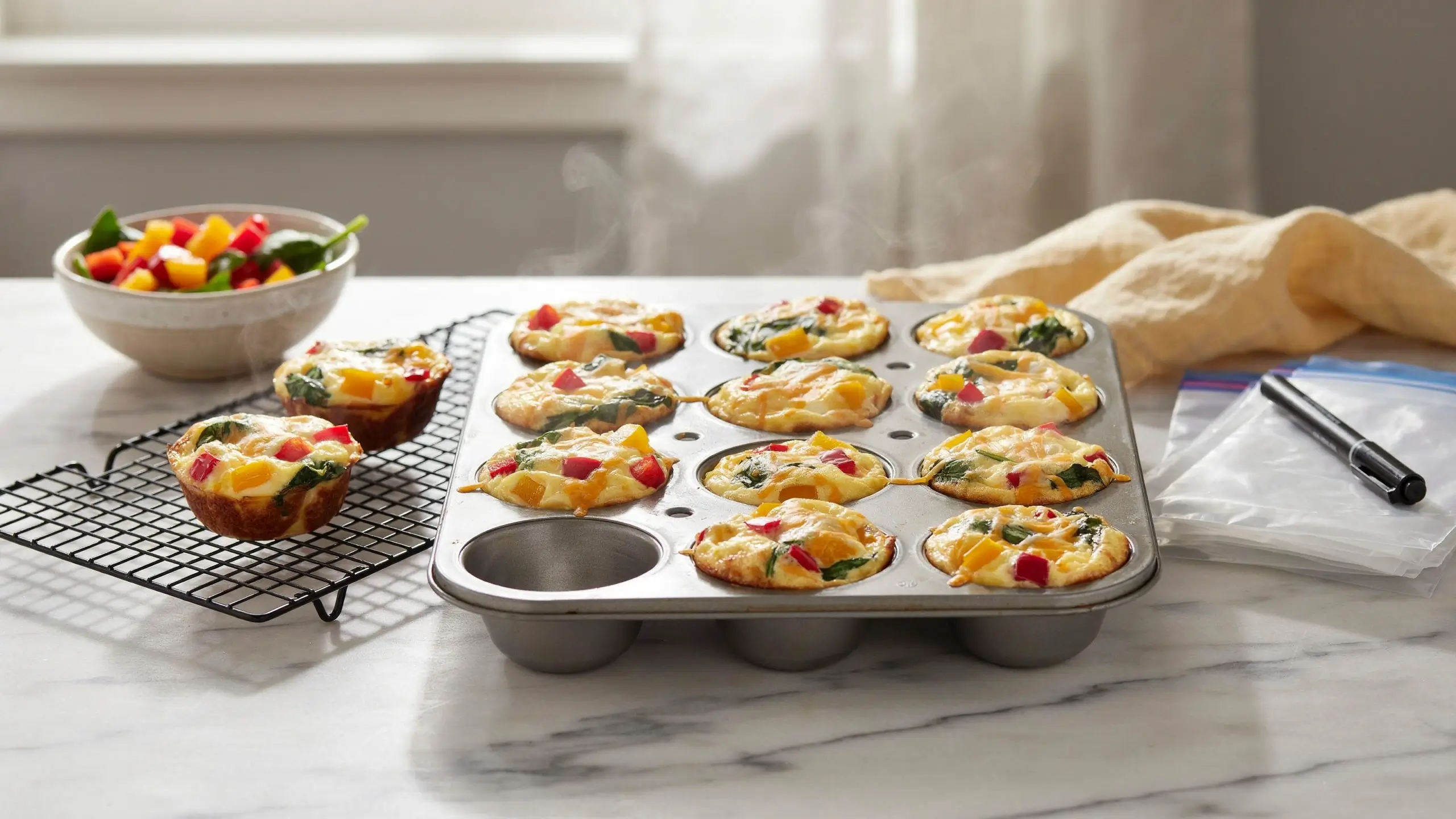 Freshly baked muffin tin egg bites with red bell peppers and spinach on a cooling rack with rising steam.