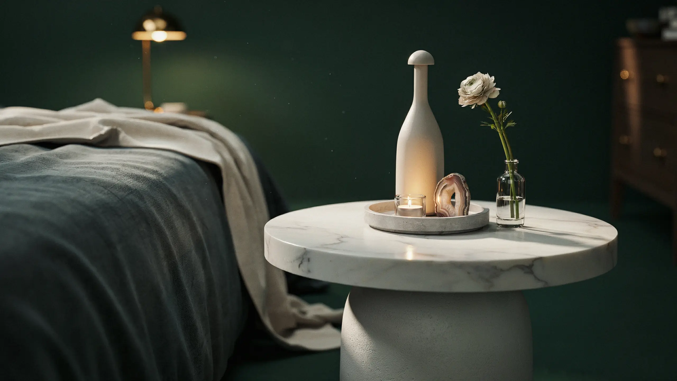Round white marble drum table with minimalist decor, candle, and white flower in a moody dark green bedroom setting. 