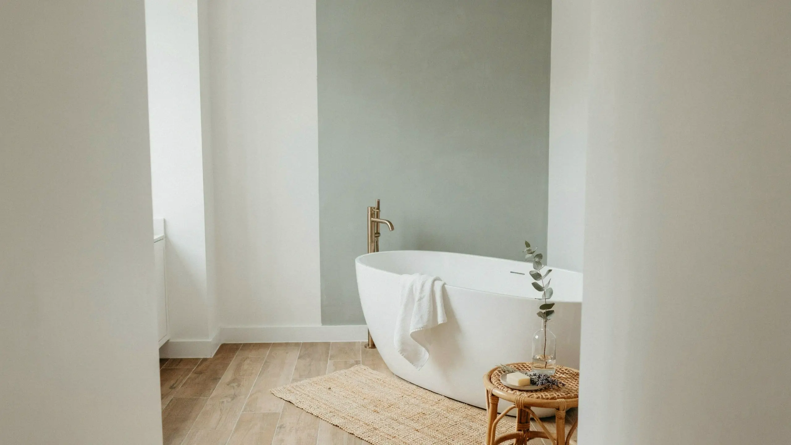 A minimalist bathroom featuring a white freestanding tub and a sage green painted accent wall.