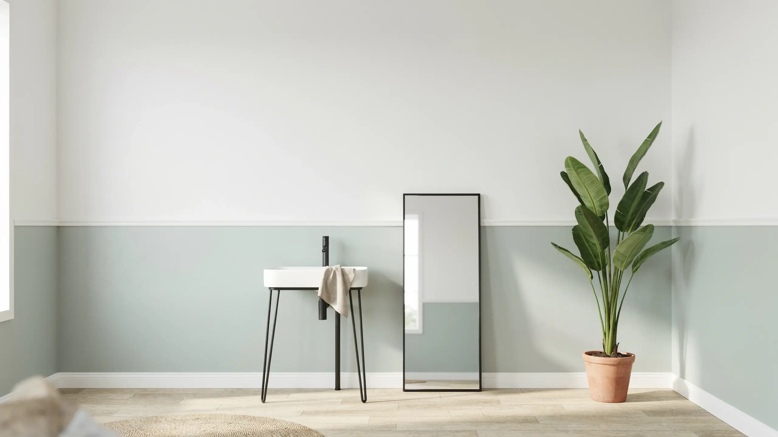 A minimalist bathroom corner featuring a sage green half-and-half painted wall, a modern freestanding white sink with black hardware, a slim black-framed floor mirror, and a tall potted plant on light wood flooring.