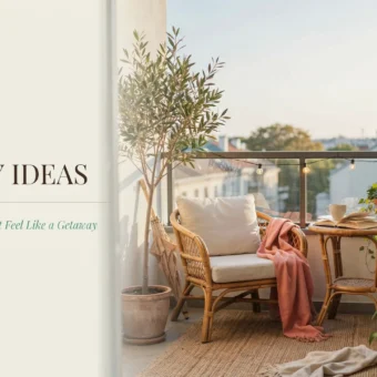 A cozy small balcony decorated with a rattan armchair, white cushions, and a pink throw blanket. An olive tree and snake plant bring greenery to the space, next to a small table holding a mug and an open book. The scene is lit by string lights with text reading "25 Small Balcony Ideas