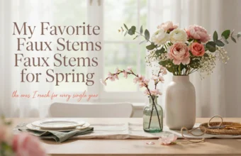 White ceramic vase holding faux pink peonies and cherry blossom stems on a bright wooden dining table with elegant spring place settings.