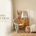 Warm, neutral boho nursery decor featuring a white crib with a cloud pillow, a hanging rattan chair draped in a beige throw, a wooden dresser with pampas grass, and soft sunlight filtering through sheer white curtains.