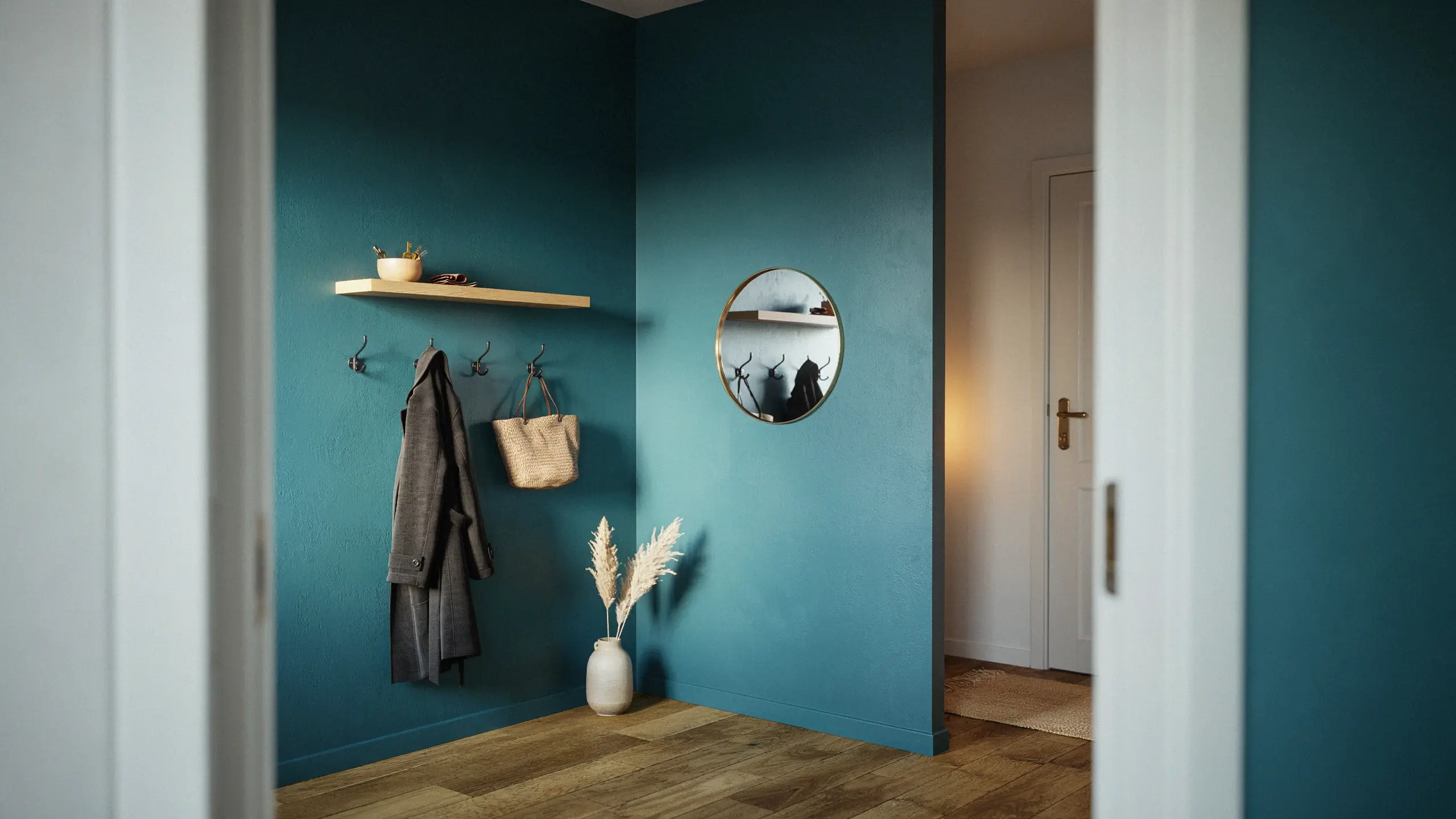 Modern entryway with a deep teal green accent wall, wooden floating shelf, round brass mirror, coat hooks, and a ceramic vase with dried pampas grass.