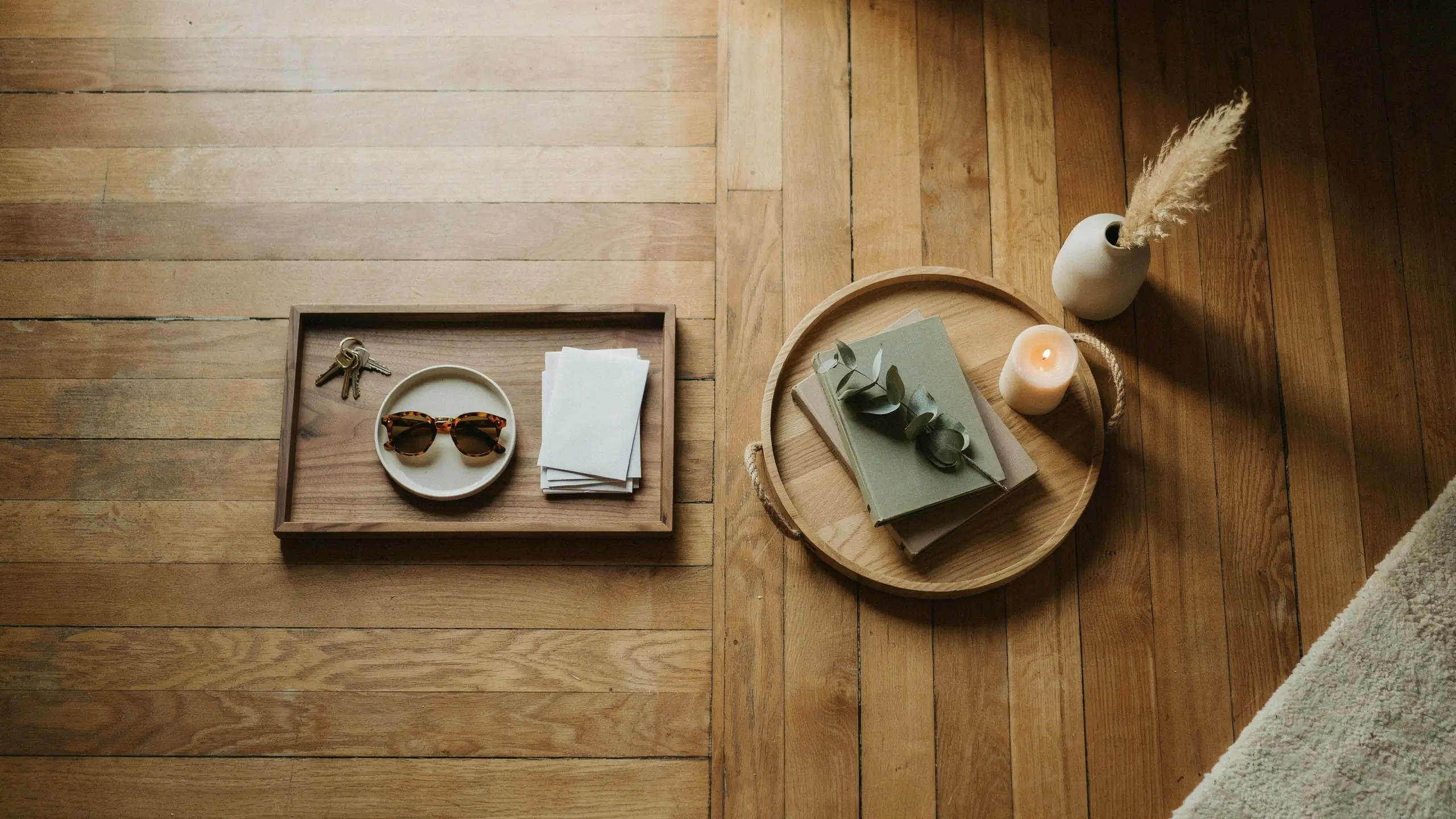 Flat lay of minimalist wooden trays, a ceramic plate, and a glass vase with pampas grass, representing eco-friendly swaps to replace plastic and wire items with organic materials.