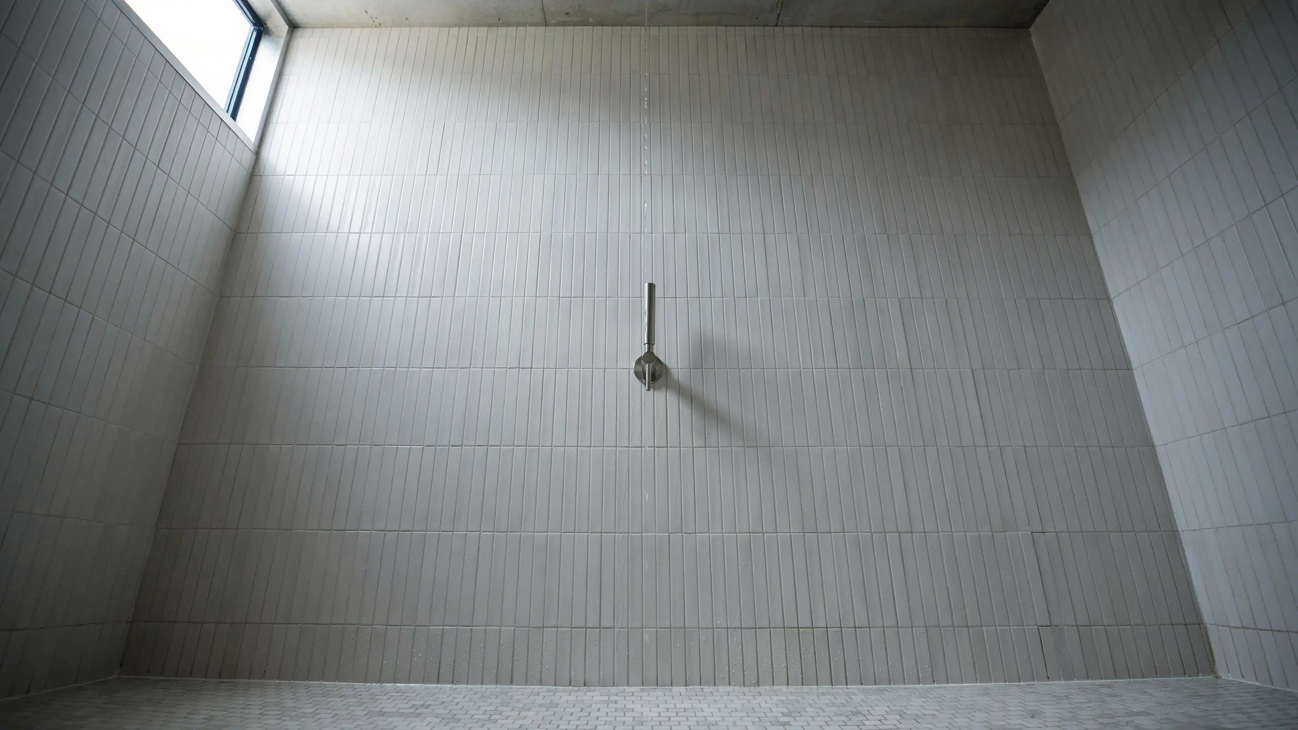 Minimalist white vertical stack shower tiles with a sleek metal shower head and bright natural light, visually elongating the room.