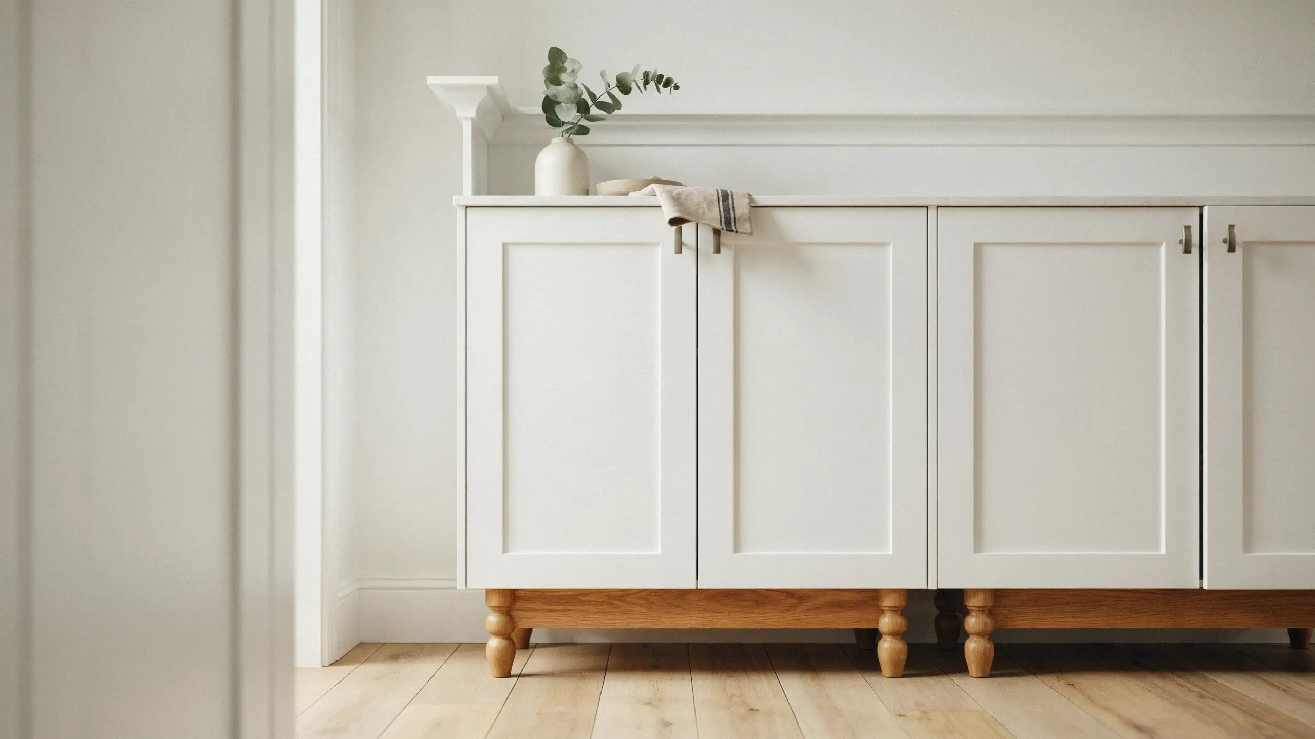 White shaker panel cabinet with turned wood legs and wainscoting trim, demonstrating how to elevate storage and avoid a boxy furniture look.