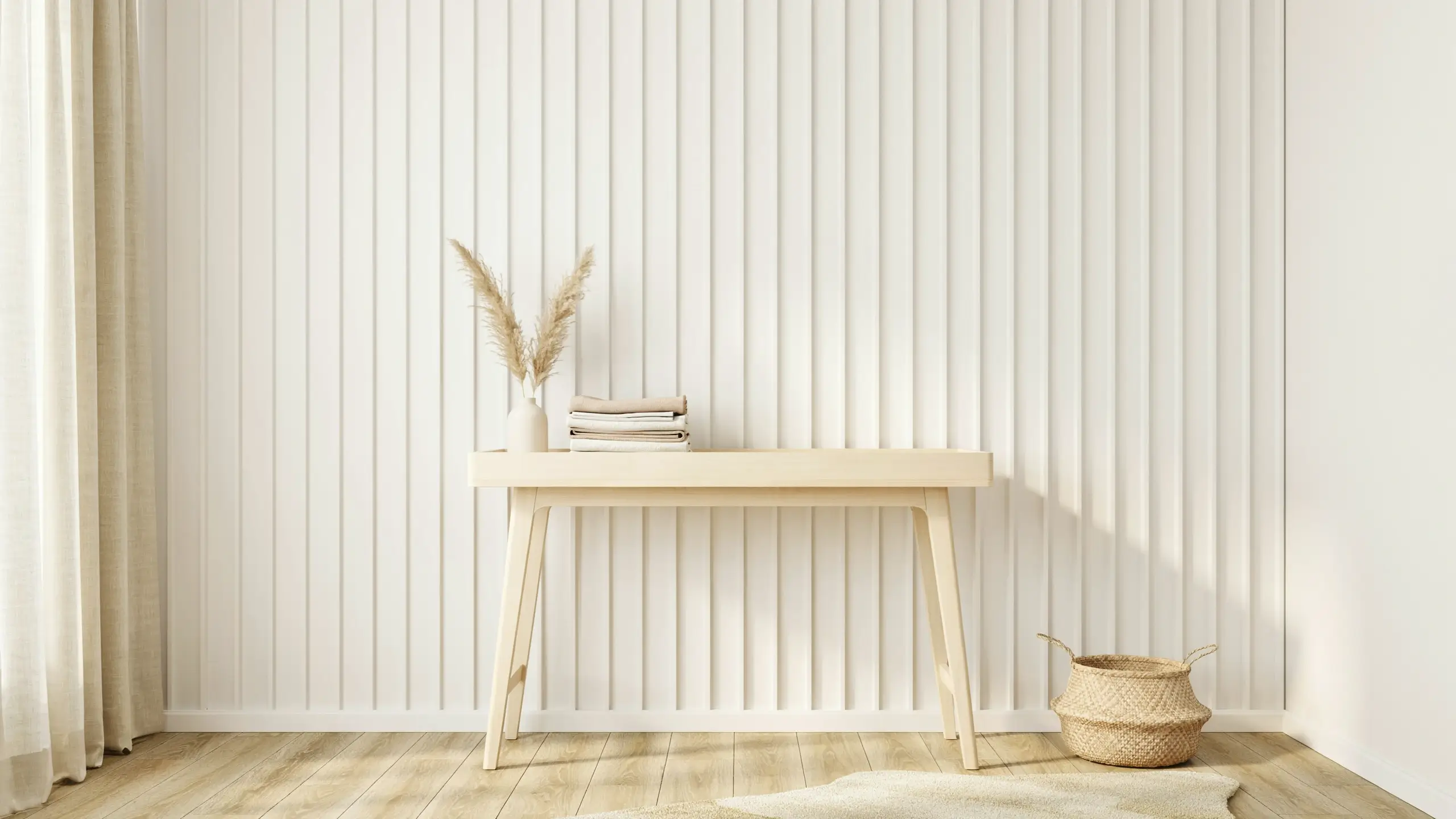 A minimalist light wood console table with pampas grass and neutral books set against a white vertical ribbed wall paneling in a sunlit room.